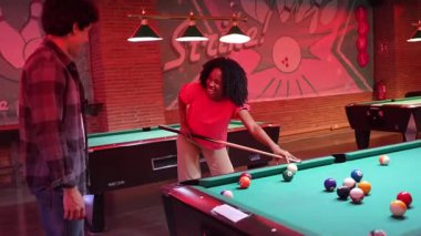 Bilardo oynayan genç bir bayan oyuncu, yavaş çekim sahnesinde hassas bir şekilde topa vuruyor loş ışıklı bovling pisti ortamında, neon ışıklı klasik iç mekan ile.