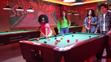 Genç, farklı arkadaşlar, loş ışıklı bilardo odasında bilardo oynuyorlar. Yavaş çekim sekansıyla, stratejik çekimler ve eğlenceli anlar yoluyla enerjik etkileşimler yakalıyorlar.