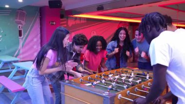 Genç yetişkinler langırt maçından zevk alıyorlar, zaferlerini coşkulu bir eğlence mekanında beşlik çakarak ve kucaklayarak kutluyorlar.