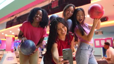 Dört farklı bayan arkadaş bowling salonunda eğlenceli anılar yakalıyor, bowling toplarıyla selfie çekiyorlar.