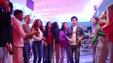 Genç arkadaşlar neşeli anları paylaşıyorlar, bovling salonunda enerji ve heyecanla dans ediyorlar, renkli neon ışıklar ve neşeli atmosfer arasında canlı ağır hareket ediyorlar.