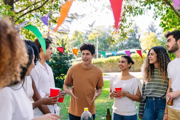 Bir grup farklı arkadaş renkli bayraklarla süslenmiş açık hava partisinde eğleniyor, konuşuyor ve eğleniyorlar.