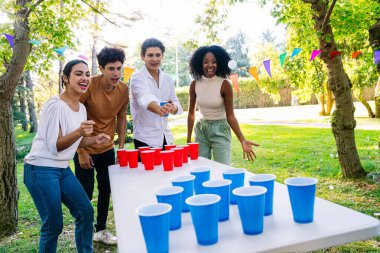 Neşeli genç yetişkinler bir parkta eğlenceli bir bira pong oyununda eğleniyor, kahkahalarımızı paylaşıyor ve yaz güneşinde neşeli anılar yaratıyorlar.