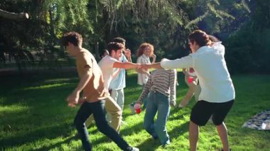 Bir grup farklı arkadaş parkta piknik yapıyor, arafta oynuyor ve ağır çekimde eğleniyorlar.