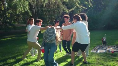 Bir grup neşeli genç arkadaş Red Rover oyunu oynuyor, yaz tatili boyunca güneşli çimlerde koşup gülüyorlar.