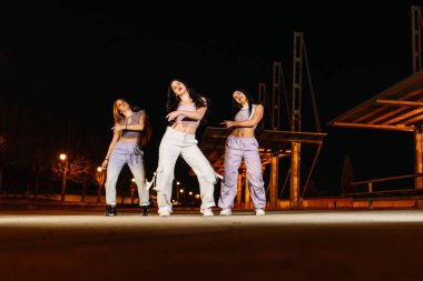 Canlı şehir sokaklarında hip hop dansı yapan bir grup genç kadın gece ışıkları altında enerji ve tutku gösterisi yapıyorlar.