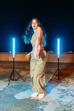 Enerjik bayan dansçı, canlı ışık altında hip hop hareketleri yapıyor, geceleri sokak dansı kültürü sergiliyor.