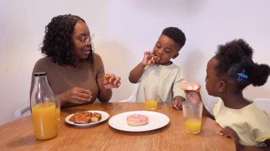 Afrikalı anne ve çocuklar evde keyifli bir kahvaltı yapıyorlar, yemeklerini paylaşıyorlar ve sıcak bir aile anı yaratıyorlar.