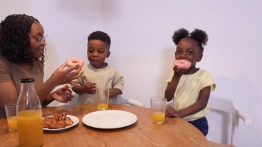 Afrikalı aile tatlı çörek anlarını paylaşıyor, portakal suyunun tadını çıkarırken aynı zamanda birlikte sabah kahvaltısının tadını çıkarıyor.