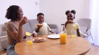 Sıcak sabah güneşi mutfak penceresinden yayılıyor, Afrikalı anne gülümseyen çocuklarla kahvaltı anlarını paylaşıyor, hamur işlerinin ve portakal suyunun keyfini çıkarırken derin bir bağ kuruyor.