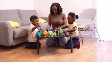 Afrikalı Amerikalı aile üyeleri renkli yapı taşlarıyla oynarken yakınlaşıyorlar, rahat oturma odası ortamında yaratıcı öğrenme aktiviteleriyle uğraşıyorlar.