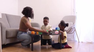 Afrikalı Amerikalı aile üyeleri renkli yapı taşlarıyla oynarken yakınlaşıyorlar, rahat oturma odası ortamında yaratıcı öğrenme aktiviteleriyle uğraşıyorlar.