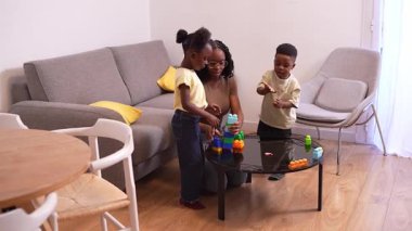 Afrikalı Amerikalı aile üyeleri renkli yapı taşlarıyla oynarken yakınlaşıyorlar, rahat oturma odası ortamında yaratıcı öğrenme aktiviteleriyle uğraşıyorlar.