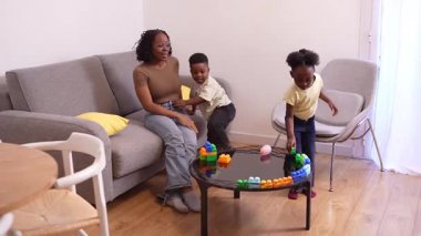 Afrikalı Amerikalı aile üyeleri renkli yapı taşlarıyla oynarken yakınlaşıyorlar, rahat oturma odası ortamında yaratıcı öğrenme aktiviteleriyle uğraşıyorlar.