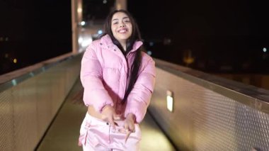 Akşamları şehrin aydınlanmış yaya köprüsünde dinamik sokak dansı hareketleri yapan yetenekli kadın dansçı ritmik hareketlerle canlı enerjiyi ifade ediyor.