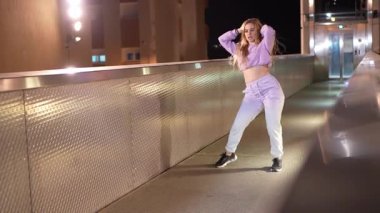 Gece vakti şehir köprüsünde dinamik sokak dansı koreografisi yapan genç bayan dansçı, modern hareket ve sanatsal ifadeyi enerji ve kendine güvenle sergiliyor.