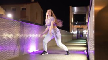 Gece vakti şehir köprüsünde dinamik sokak dansı koreografisi yapan genç bayan dansçı, modern hareket ve sanatsal ifadeyi enerji ve kendine güvenle sergiliyor.