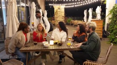 Genç yetişkinler şehrin çatı katındaki barda neşeli anlar paylaşıyorlar, gece ışıkları altında içkinin tadını çıkarırken canlı sohbetler yapıyorlar.