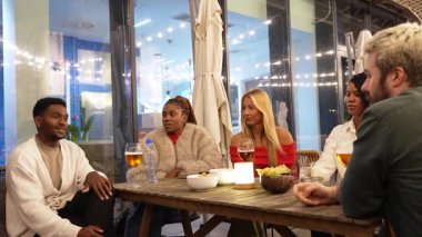 Çok ırklı arkadaşlar, sıcak kentsel mekanda sıcak gece toplantıları sırasında gülüp kokteyller içerek animasyon hikayelerini paylaşıyorlar.