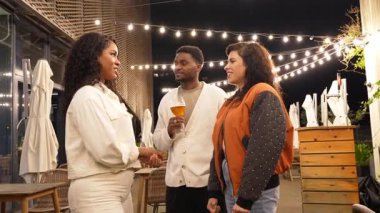 Çeşitli arkadaş gurubu güler, sohbet eder, partilerin ışıkları altında canlı bir sosyal etkinlik sırasında içkinin tadını çıkarırlar.