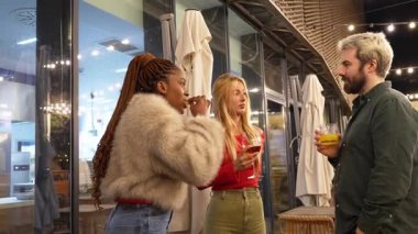 Arkadaşlar akşam içkilerinin tadını çıkarırken gülüşlerini paylaşıyorlar, sosyal bağları ve gece hayatı arkadaşlığını neşeli bir şekilde vurguluyorlar.