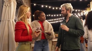 Yetişkin genç arkadaşlar gece kulübünde toplanıyor, neşeli sohbetler, içkiler ve kahkahalar paylaşıyorlar.