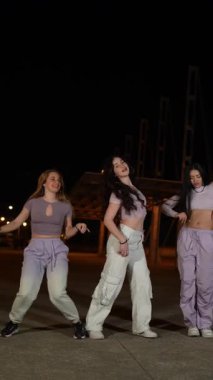 Kadın dans ekibi şehir ışıkları altında enerjik sokak dansları yapıyor. Şehir dans kültürünü ve yaratıcı hareketlerini sergiliyor.