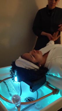 Modern bir güzellik kliniğinde basınçlı su masajıyla rahatlatıcı bir saç tedavisiyle rahatlama ve gençleştirme sağlayan bir kadın.