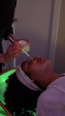 Güzellik uzmanının güzellik tedavisi sırasında müşterinin yüzüne krem maske takması.