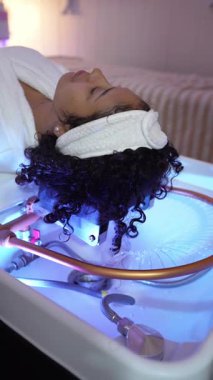 Sakin bir güzellik kliniğinde, basınçlı suyla rahatlatıcı bir saç masajı yapan genç bir kadının ağır çekimde...