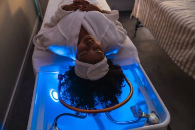 Huzurlu bir hasta tedavi edici bir su yatağı tedavisi görüyor. Sakinleştirici mavi ışıklarla iyileştiriliyor. Rahatlamayı ve modern bir spa ortamında olmayı teşvik ediyor.