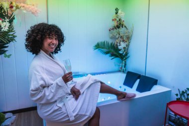 Genç bir kadın modern bir kaplıcada dinlenmenin keyfini çıkarıyor, hidromasaj havuzunda şampanya yudumluyor.