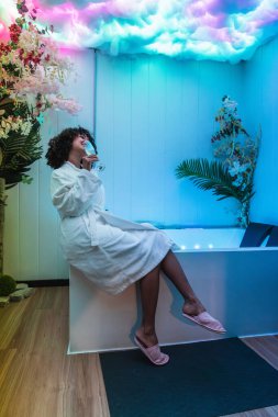 Sakin renkler ve çiçek dekoru ile çevrili bir kaplıcada huzurlu bir anın tadını çıkaran kadın rahatlama ve refahı teşvik ediyor.