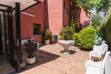 Huzurlu bir açık teras bir huzurevinde, banklar, saksı bitkileri, ve merkezi bir çiçek yatağı, sakinleri için huzurlu bir yer sağlar.