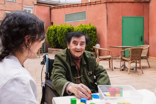 Yaşlı bir kadın dışarıda bir bakıcıyla terapi aktivitesinden zevk alıyor. Bakıcı ile bir huzurevinde bağlantı kuruyor ve zihinsel uyarılma sağlıyor.