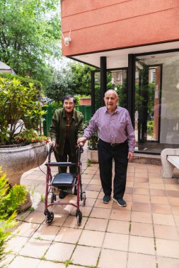 Hemşire, Walker 'a bahçedeki bakımevinde yardım ediyor. Hareket kabiliyeti ve refahı arttırıyor.