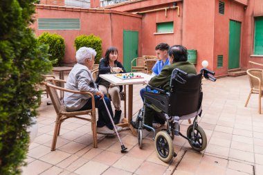 Hemşireler yaşlılarla ilgileniyor, bir huzurevinin avlusunda masa oyunu oynuyorlar.