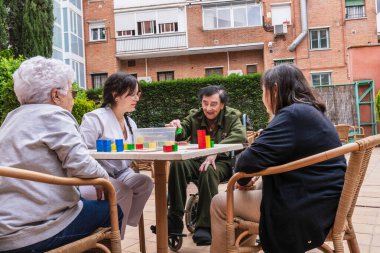 Dışarıda sosyal aktiviteden hoşlanan yaşlı kadınlar, bir huzurevi avlusunda renkli blokları olan binalar, cemaati teşvik etmek ve etkileşim kurmak.