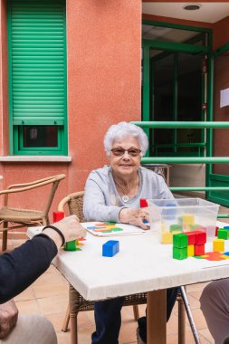 Üst düzey bir kadın açık hava bakımevinde blok oyunundan zevk alıyor, sosyal etkileşimi teşvik ediyor ve canlı bir ortamda bilişsel bağlılık sağlıyor.