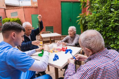 Hemşire, açık bir bakımevinde renkli inşaat oyuncaklarıyla oynayan yaşlı insanlara yardım ediyor, bilişsel becerileri ve sosyal etkileşimi teşvik ediyor.