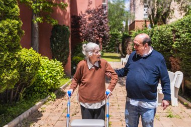 Sunny Huzurevi bahçesinde yaşlı bir kadına Walker 'a yardım eden aile destek ve bakım sağlıyor.