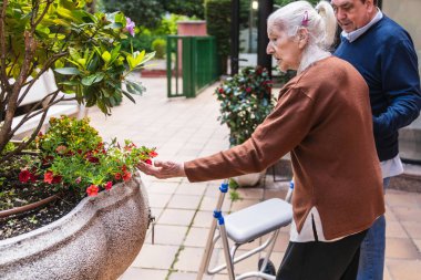 Aile ve kıdemli bir kadın, bir bakıcının yardımıyla, açık bir bakımevinde çiçeklerle ilgileniyor. Terapi amaçlı bahçıvanlık faaliyetlerine odaklan.