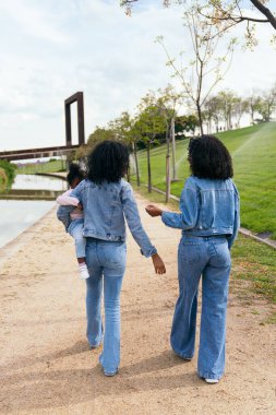 Parkta kızıyla yürüyen iki anne aynı kot ceketleri giyerek, dışarıda ailecek vakit geçirmenin tadını çıkarıyorlar.