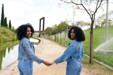 Kot ceket ve kot pantolon giyen iki ikiz kardeş el ele tutuşup parkta birlikte vakit geçiriyorlar.