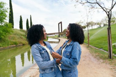 İki neşeli ikiz kardeş kot ceket giyip Madrid, İspanya 'da popüler bir eğlence alanı olan Madrid Rio Park' ta kucaklaşıp gülüşüyorlar.