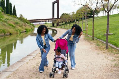 Afrikalı iki ikiz kardeş güneşli bir günün tadını çıkarıyorlar. Yeğenlerini bir bebek arabasıyla kanalda gezdiriyorlar.