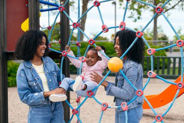 İkiz kardeşler oyun alanında yeğenleriyle gülüp oynuyorlar. Güneşi emerek birlikte neşeli anılar yaratıyorlar.