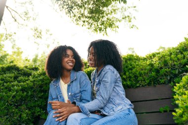 İki ikiz kardeş parkta bir bankta oturuyor, birlikte vakit geçiriyorlar ve yeşillikler arasında bir bağ kuruyorlar.
