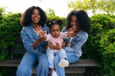 İkiz kardeşler gülümsüyor ve yeğenlerini kucaklıyorlar. Parkta güneşli bir günün tadını çıkarırken birlikte neşeli anılar yaratıyorlar.