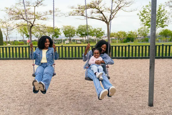 Anne ve teyze, oyun parkında salıncakta yeğenleriyle oynaşıp güneşin altında neşeli anılar yaratıyorlar.